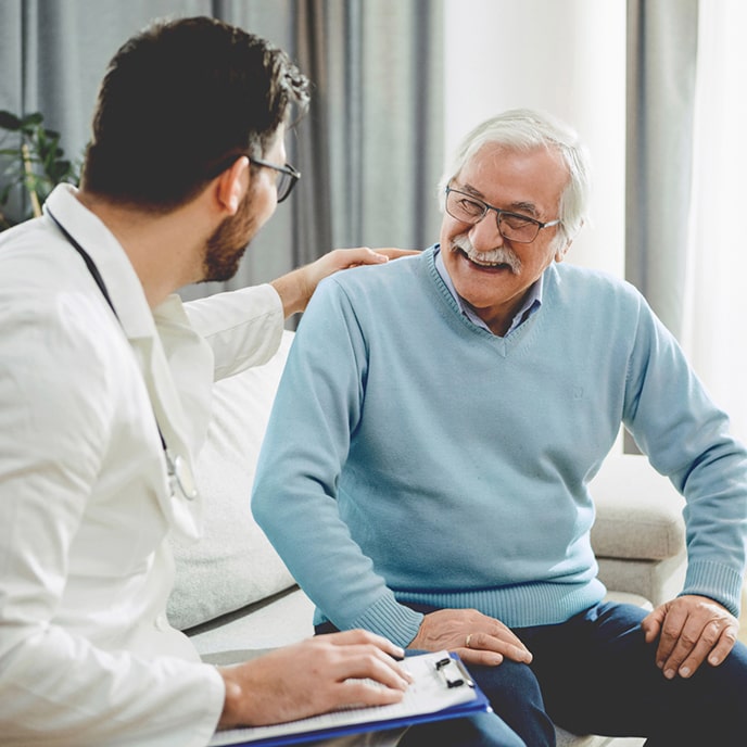 A doctor and his patient sitting on a sofa smiling.