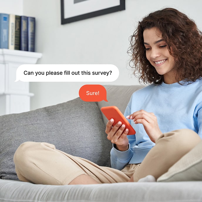 A woman sitting on a couch, answering a survey on her cellphone
