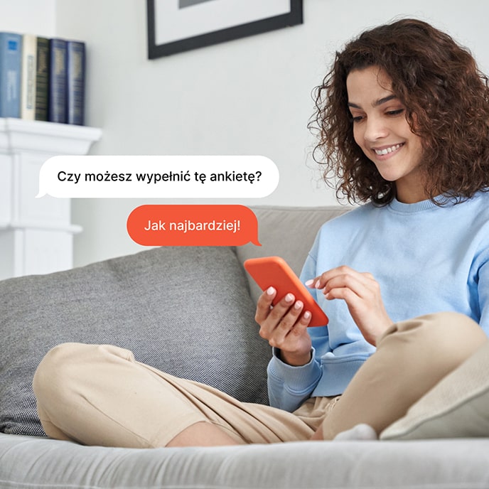 Dziewczyna siedząca na kanapie i odpowiadająca na ankietę w telefonie komórkowym